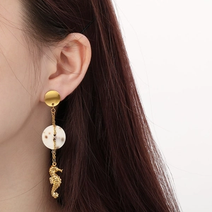 Close-up of model wearing gold seahorse drop earrings with shell disc and pearl accents