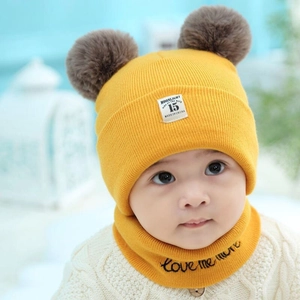 Detail of yellow baby knit hat with double pom-poms and matching scarf with embroidery