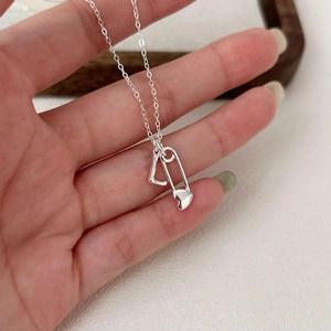 Detail of 925 sterling silver necklace featuring a heart safety pin and L-letter pendant