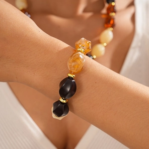 Detailed view of amber and black acrylic faceted beads with gold spacers on wrist