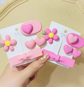 Close-up of pink hair clips set featuring heart, flower and bow resin decorations on a card