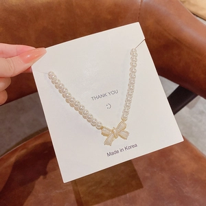 Close-up of a Korean style pearl necklace featuring a golden bow pendant on a card