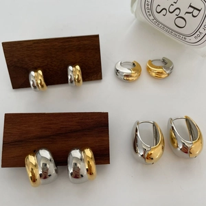 Modern two-tone gold and silver C-shaped teardrop hoop earrings on wooden stand