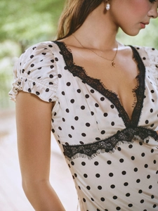 Detailed view of beige polka dot dress with black lace trim and sexy V-neck design
