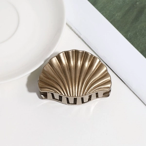 Top view of a gold shell hair claw clip on a white surface with decorative props