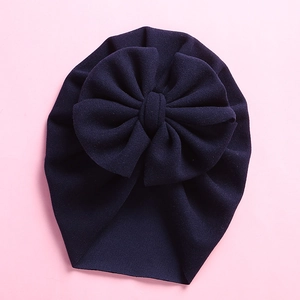 Close-up of a dark blue baby turban hat with a large bow on a soft pink background