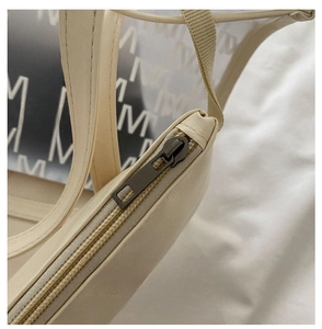 Detail shot of vintage bronze zipper and textured cream leather tote with M pattern
