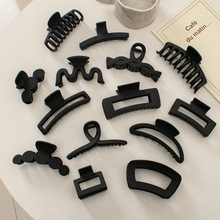 Flat lay of 12 matte black hair claw clips in various geometric shapes on white desk