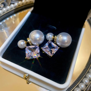 Macro detail of 18k gold plated double pearl earrings with square zircon on velvet