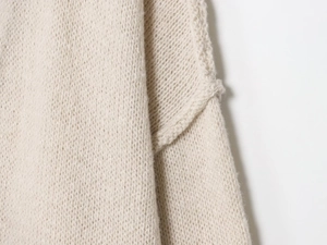 Dettaglio della trama a maglia grossa e del tessuto di un cardigan color crema avena