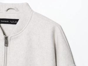 Close-up of soft grey bomber jacket collar with a silver metal zipper and woven neck label
