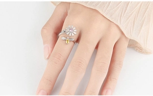 Detail of adjustable silver flower ring with daisy and bee motif worn by a model