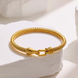 Detail of golden cable twist bangle with hook clasp on textured white stone