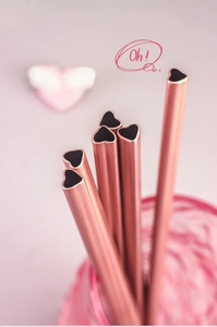 Macro view of rose gold heart-shaped stainless steel straws in a pink cup