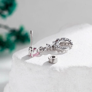 Silver crescent moon and pink heart stone earring stud on a white textured stone