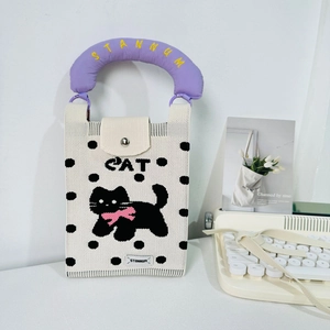 Close-up of knit cat bag with purple strap and pink bow detail on cream fabric