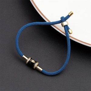 Close-up of blue braided evil eye bracelet with gold accents on a textured black surface