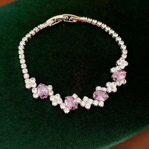 Detail view of gold-tone zircon bracelet with purple oval stones on green velvet surface