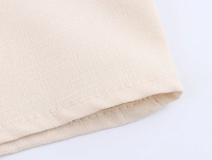 Detailed macro view of beige linen fabric texture and double-stitched hem on the shirt