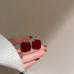 Close-up of vintage square red enamel earrings with gold trim held by hand