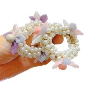 Handheld view of a pair of elastic hair ties with white faux pearls and fabric flowers