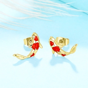 Macro shot of gold koi earrings with red enamel and zircon on a light blue base