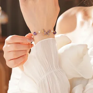Elegant gold butterfly bracelet with purple crystals and white pearls on woman's wrist