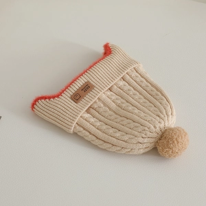 Detail of beige knit baby hat with red faux fur trim and cozy leather logo patch