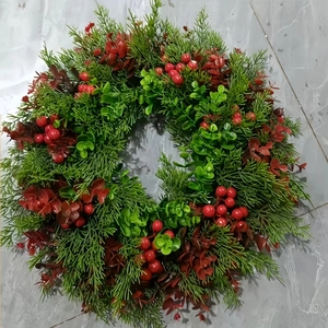 Detailed close-up of artificial Christmas wreath with green cypress leaves and red berries