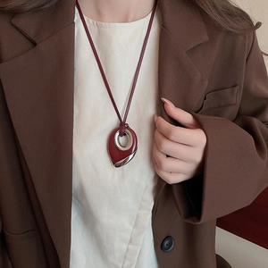 Detail of burgundy leather lanyard necklace with oval silver metal and red lacquered pendant