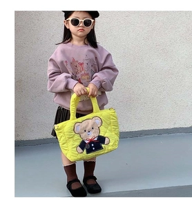 Close-up of a quilted yellow kids shoulder bag with a cute cartoon bear embroidery