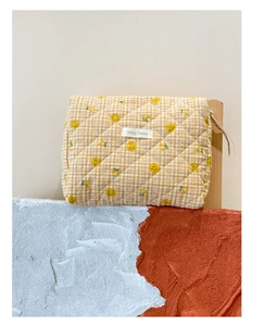 Détail d'une trousse à maquillage matelassée jaune à fleurs avec étiquette jolly house