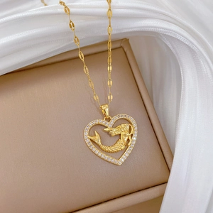 Close-up of golden mermaid heart pendant with cubic zirconia on silk background