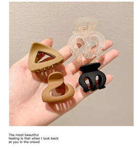Set of four matte and clear hair claws in earth tones shown being held by a hand