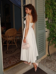 Détail d'une robe en coton blanc avec nœuds aux épaules et sac rose à texture d'autruche