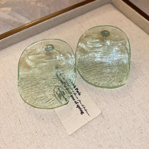 Detail view of light green irregular resin earrings with brushed texture on linen tray
