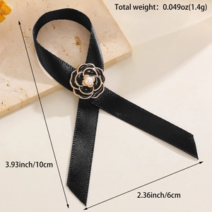 Détail d'une broche ruban noir avec fleur de camélia bordée d'or et perle centrale