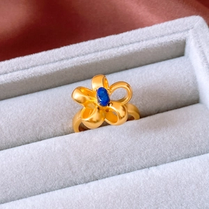 Close-up of vintage flower ring with matte gold petals and blue gemstone in a jewelry box