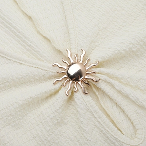 Détail de la boucle en métal doré soleil sur le tissu plissé blanc de la robe