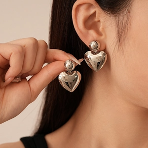 Close-up of polished silver metal heart earrings with spherical studs on a model