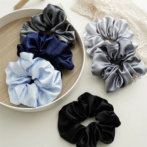 Close-up of assorted satin hair scrunchies in cool tones displayed on a wooden tray