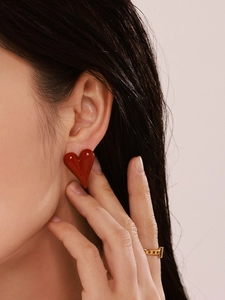 Close-up of a large red enamel heart earring and gold chain ring on a model