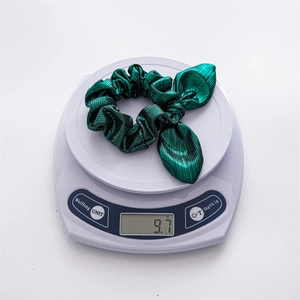 Detailed view of green bow hair scrunchie weighing 9.7g on a white digital scale
