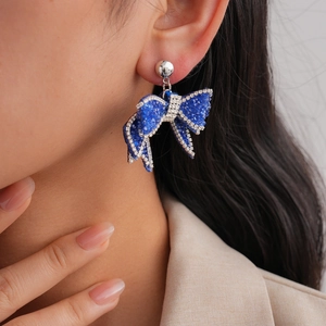 Close-up of elegant blue bow earrings with sparkling pavé crystals on a female model