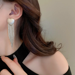 Macro detail of silver heart tassel earrings worn by a model showing long chain drapes