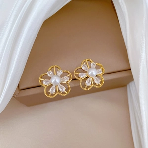 Close-up of gold hollow flower earrings with sparkling crystals and white pearls