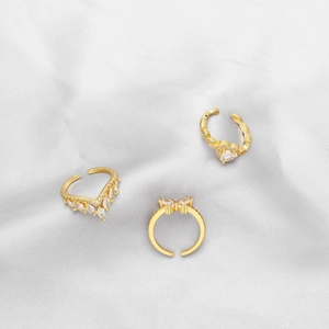 Detailed macro of adjustable golden rings with white zircons on white silk background
