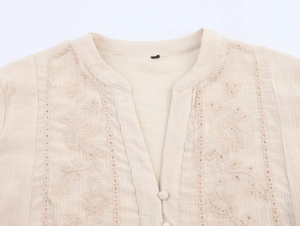 Detail of apricot embroidered cotton shirt featuring V-neckline and intricate floral texture