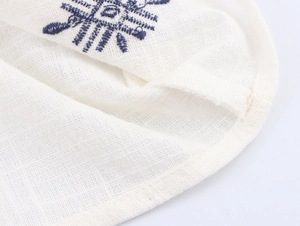Detailed macro view of cream cotton-linen fabric with blue embroidery and edge stitching
