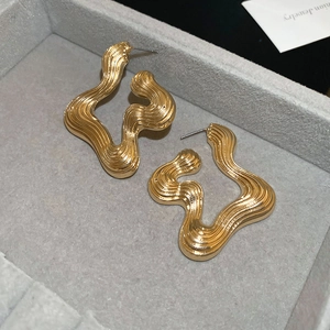 Detail showing irregular wavy gold earrings with vertical stripe texture on grey velvet box